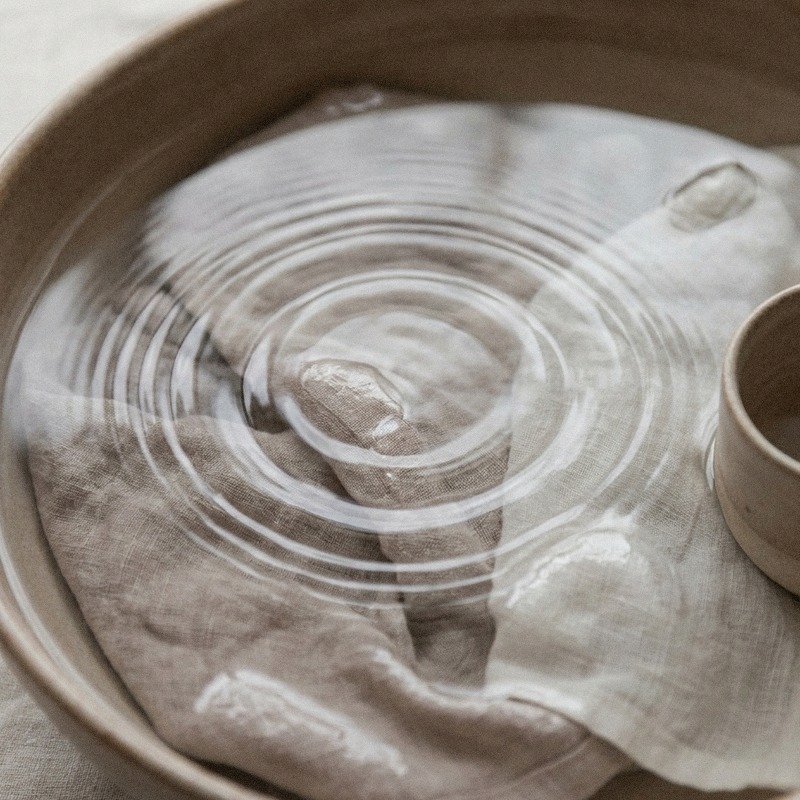 Water rippling over pale linen in a ceramic basin