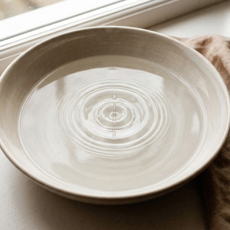 A water droplet creating concentric ripples in a pale ceramic basin